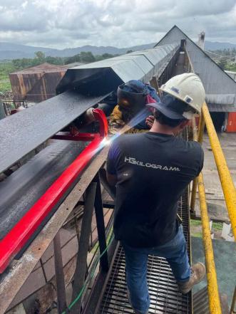 Technician installing a red weighing component on an elevated industrial conveyor